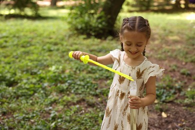 Photo of Cute little girl having fun with soap bubbles in park, space for text