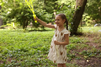 Photo of Cute little girl having fun with soap bubbles in park