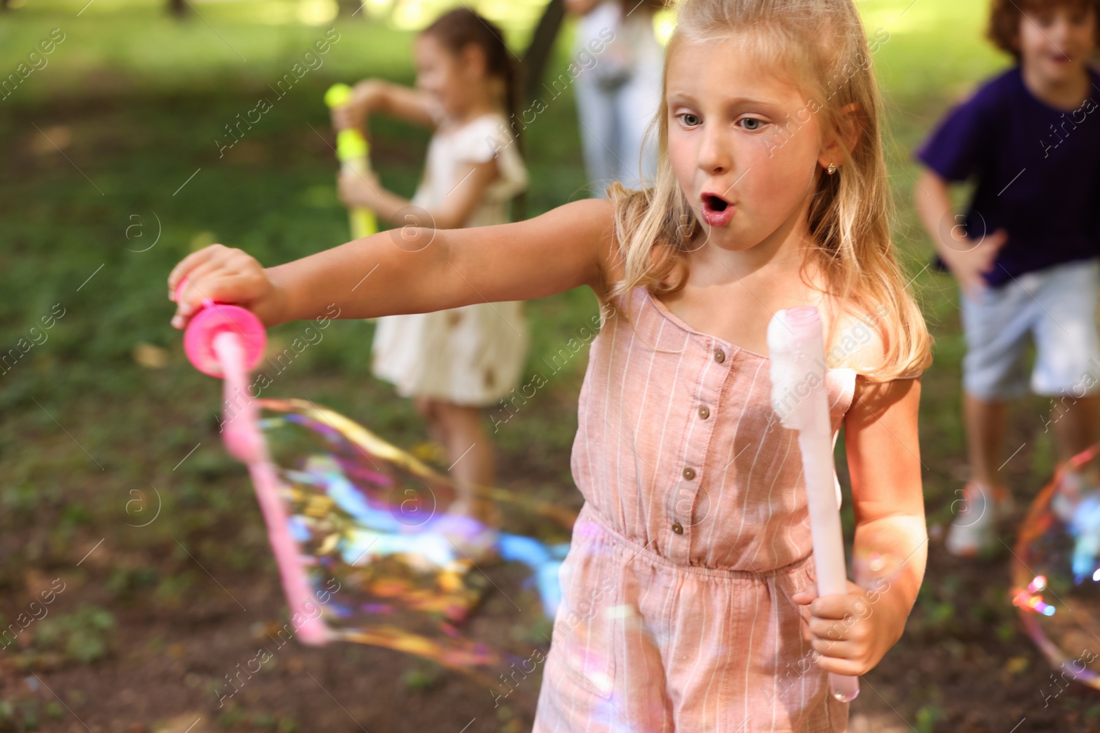 Photo of Cute little kids having fun with soap bubbles in park, selective focus