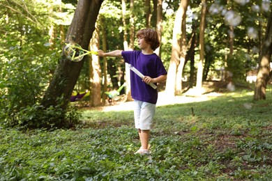Photo of Cute little boy having fun with soap bubbles in park