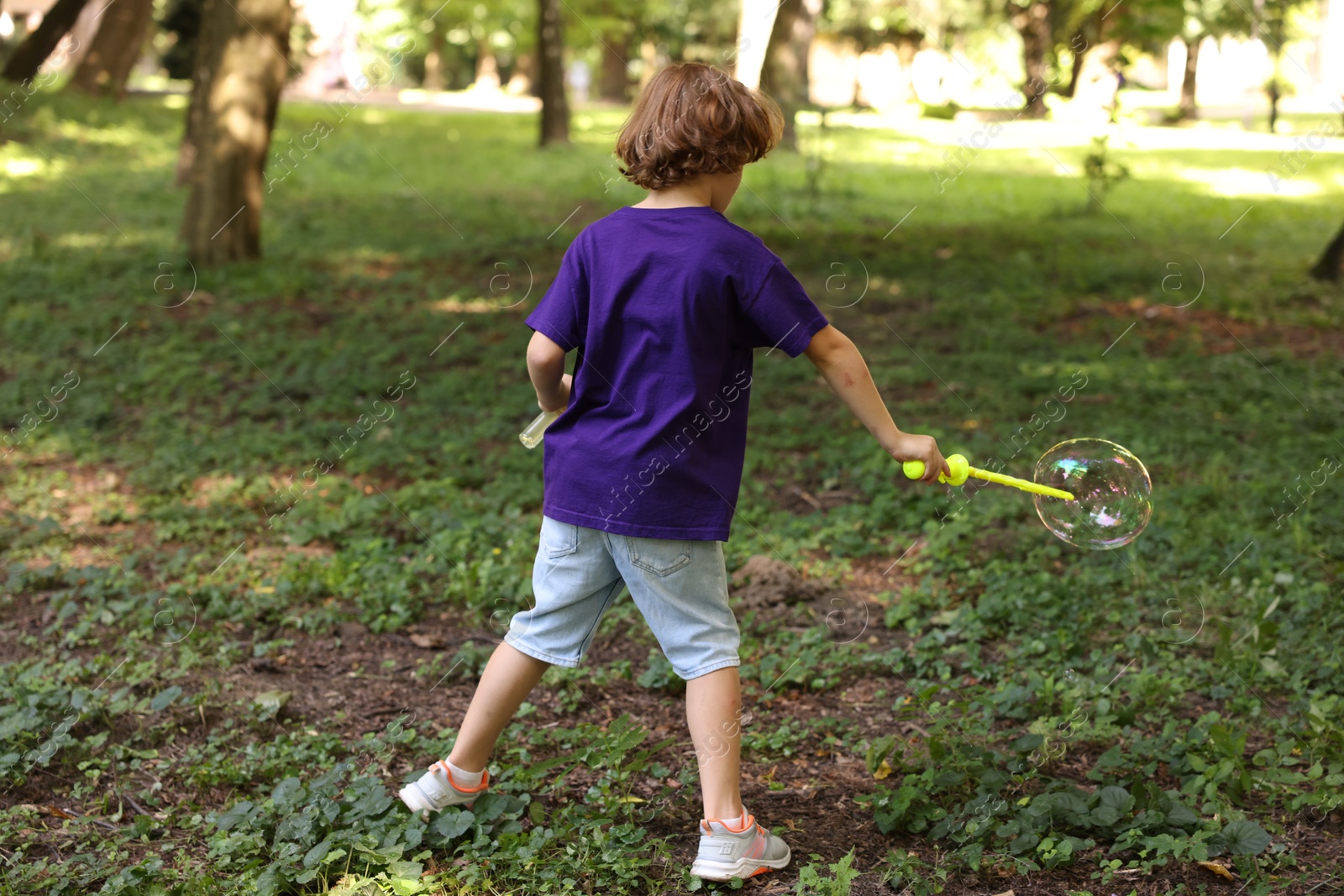 Photo of Cute little boy with bubble wand in park, back view