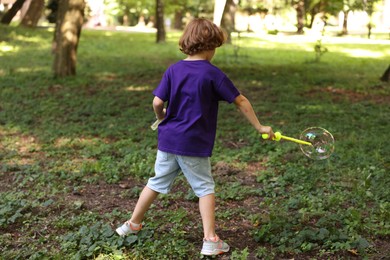 Photo of Cute little boy with bubble wand in park, back view