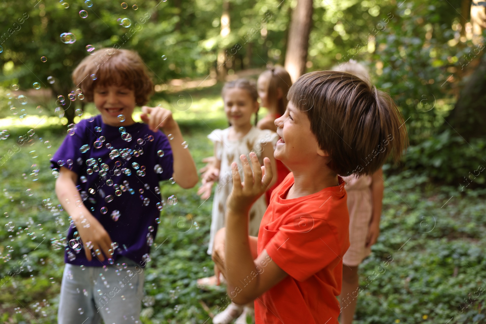 Photo of Cute little kids having fun with soap bubbles in park, selective focus
