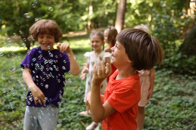 Photo of Cute little kids having fun with soap bubbles in park, selective focus