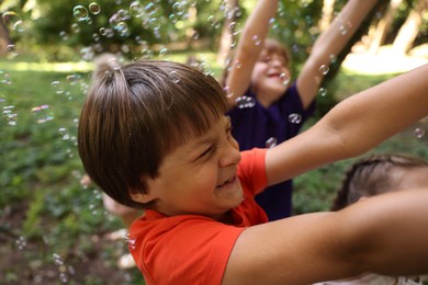 Photo of Cute little kids having fun with soap bubbles in park, selective focus