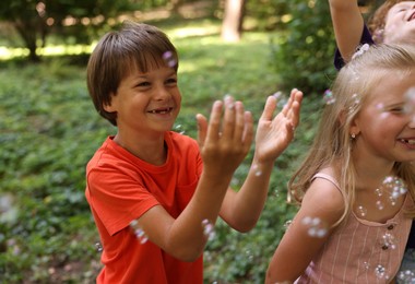 Photo of Cute little kids having fun with soap bubbles in park