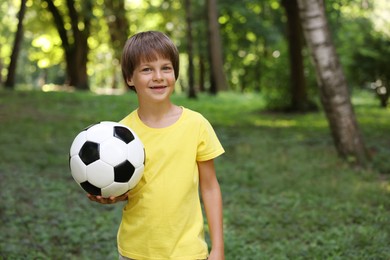 Photo of Cute little boy with soccer ball in park, space for text