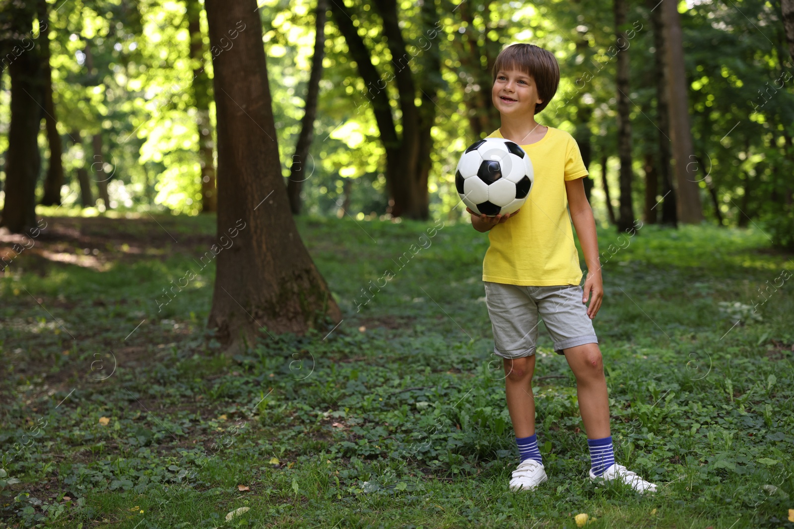 Photo of Cute little boy with soccer ball in park, space for text
