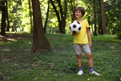 Photo of Cute little boy with soccer ball in park, space for text