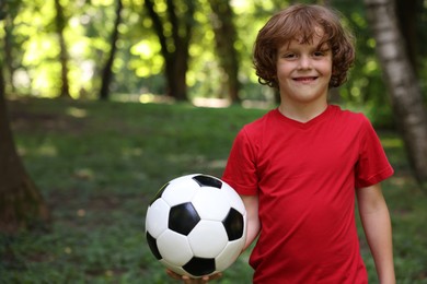 Photo of Cute little boy with soccer ball in park, space for text