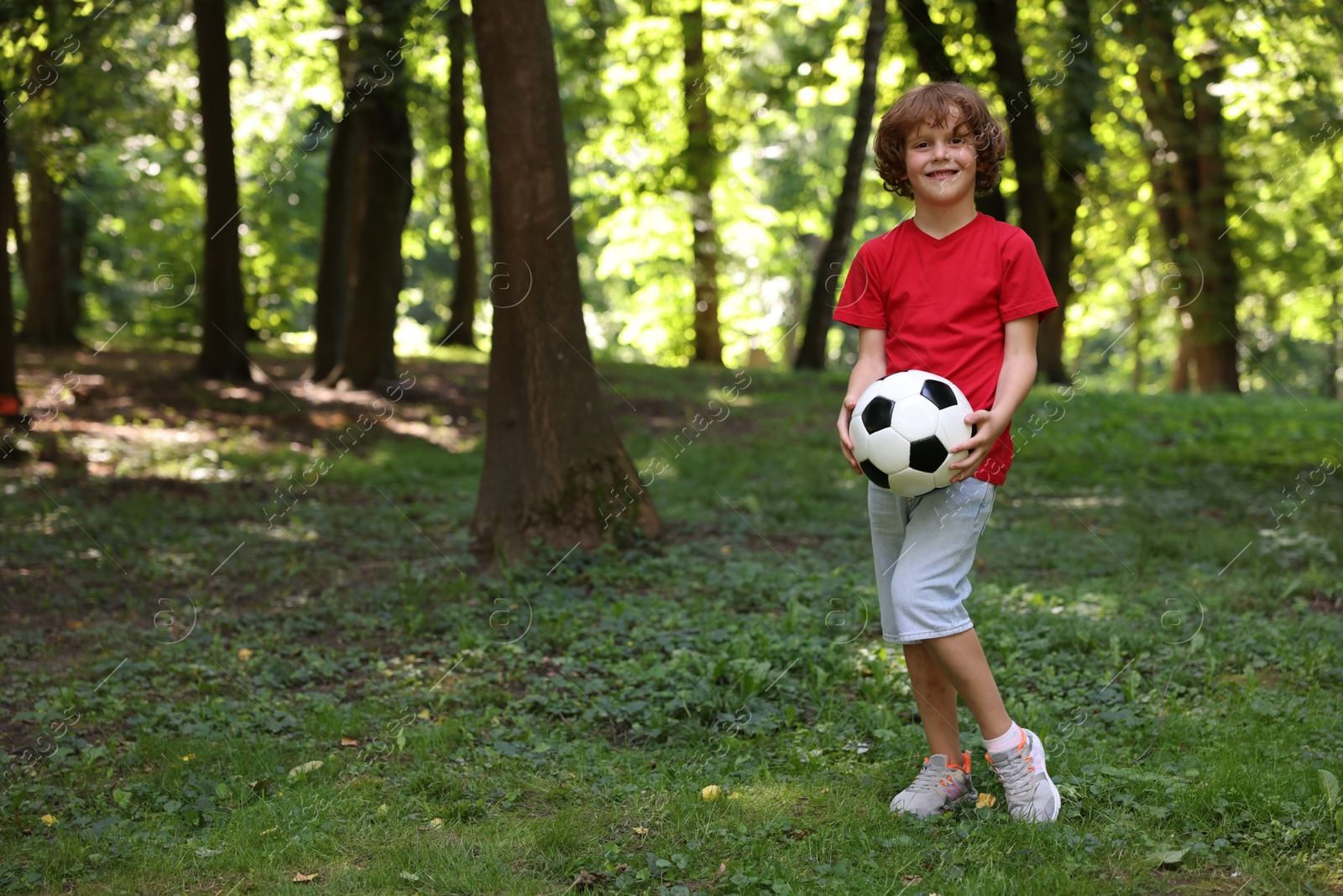 Photo of Cute little boy with soccer ball in park, space for text
