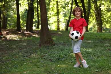 Photo of Cute little boy with soccer ball in park, space for text