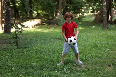 Photo of Cute little boy playing with soccer ball in park, space for text