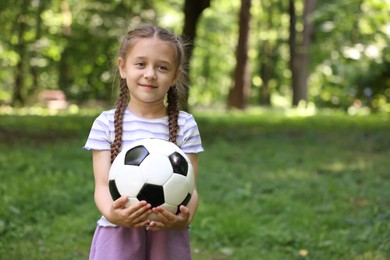 Photo of Cute little girl with soccer ball in park, space for text