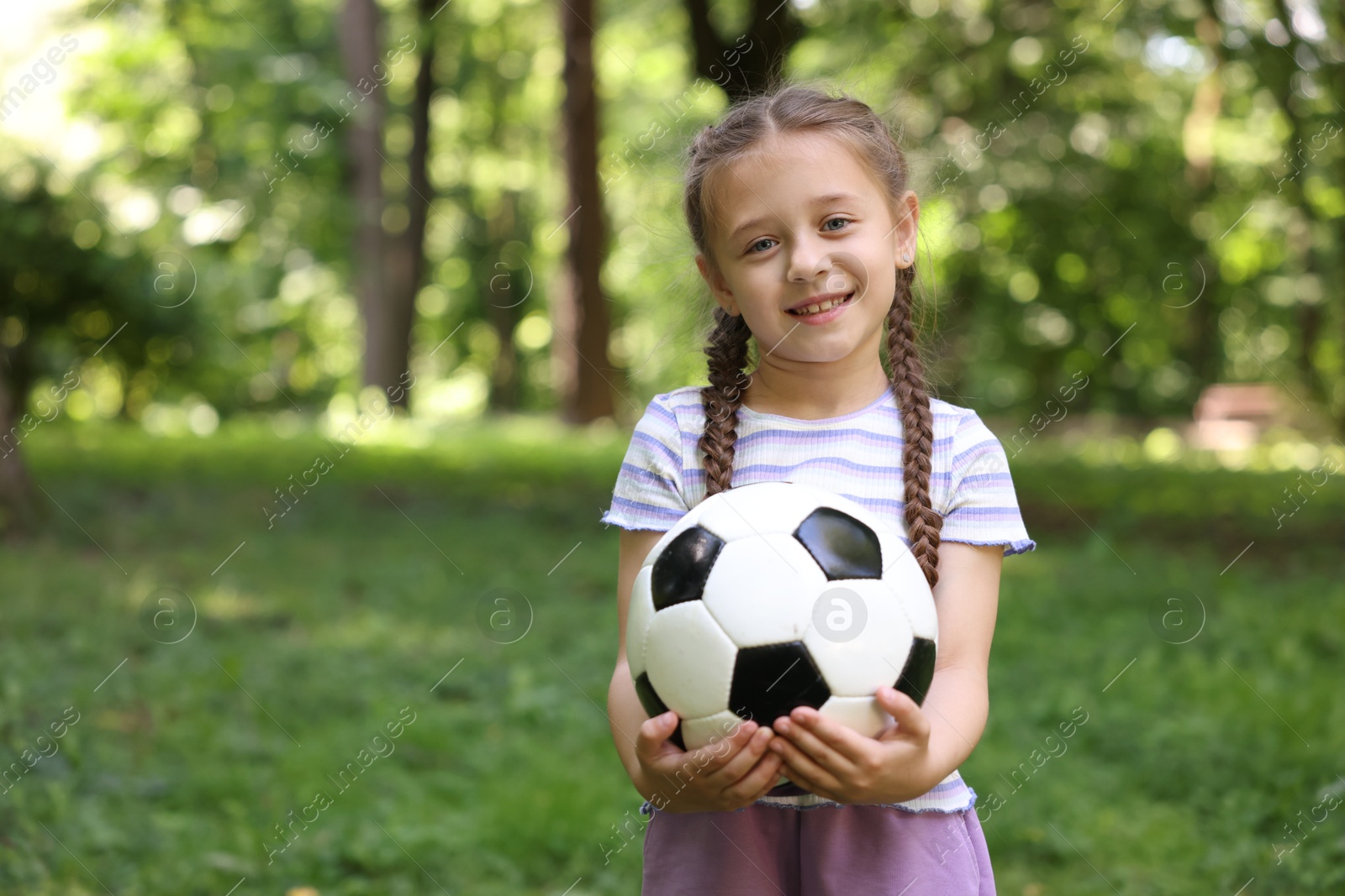 Photo of Cute little girl with soccer ball in park, space for text