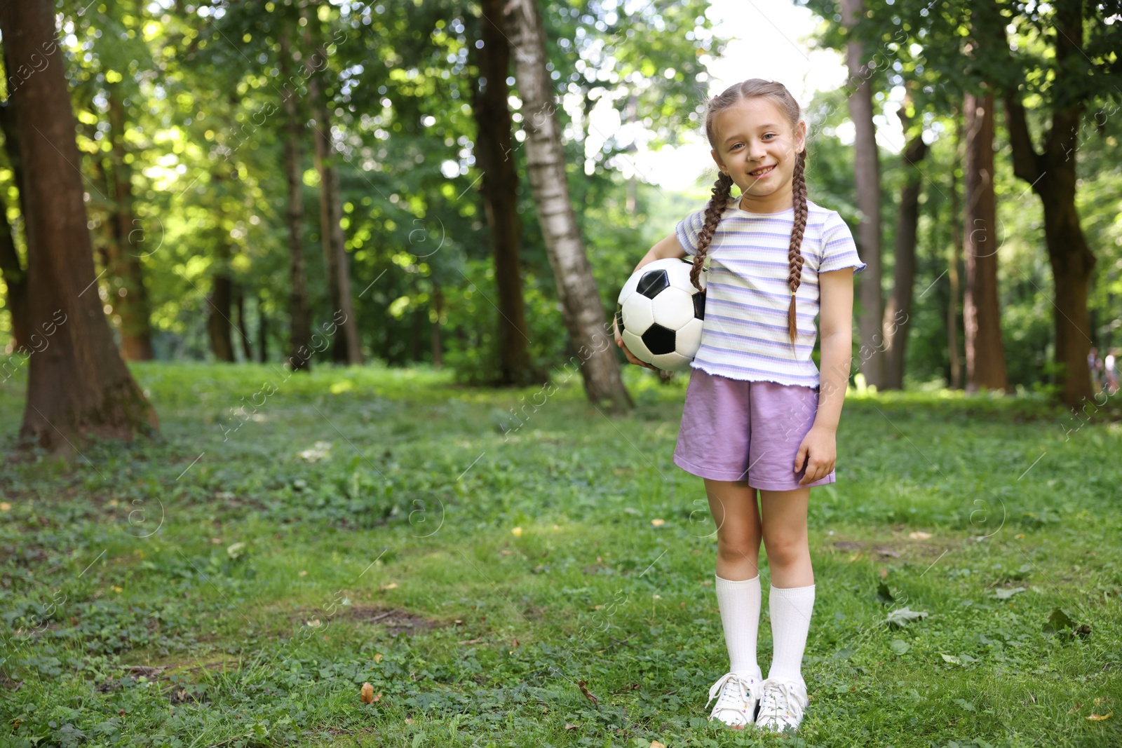 Photo of Cute little girl with soccer ball in park, space for text