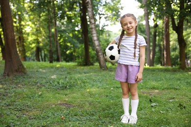 Photo of Cute little girl with soccer ball in park, space for text