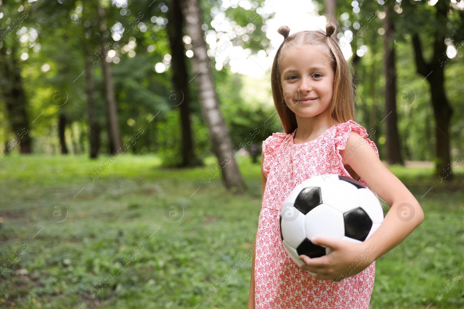 Photo of Cute little girl with soccer ball in park, space for text