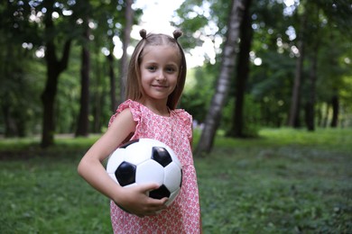 Photo of Cute little girl with soccer ball in park, space for text