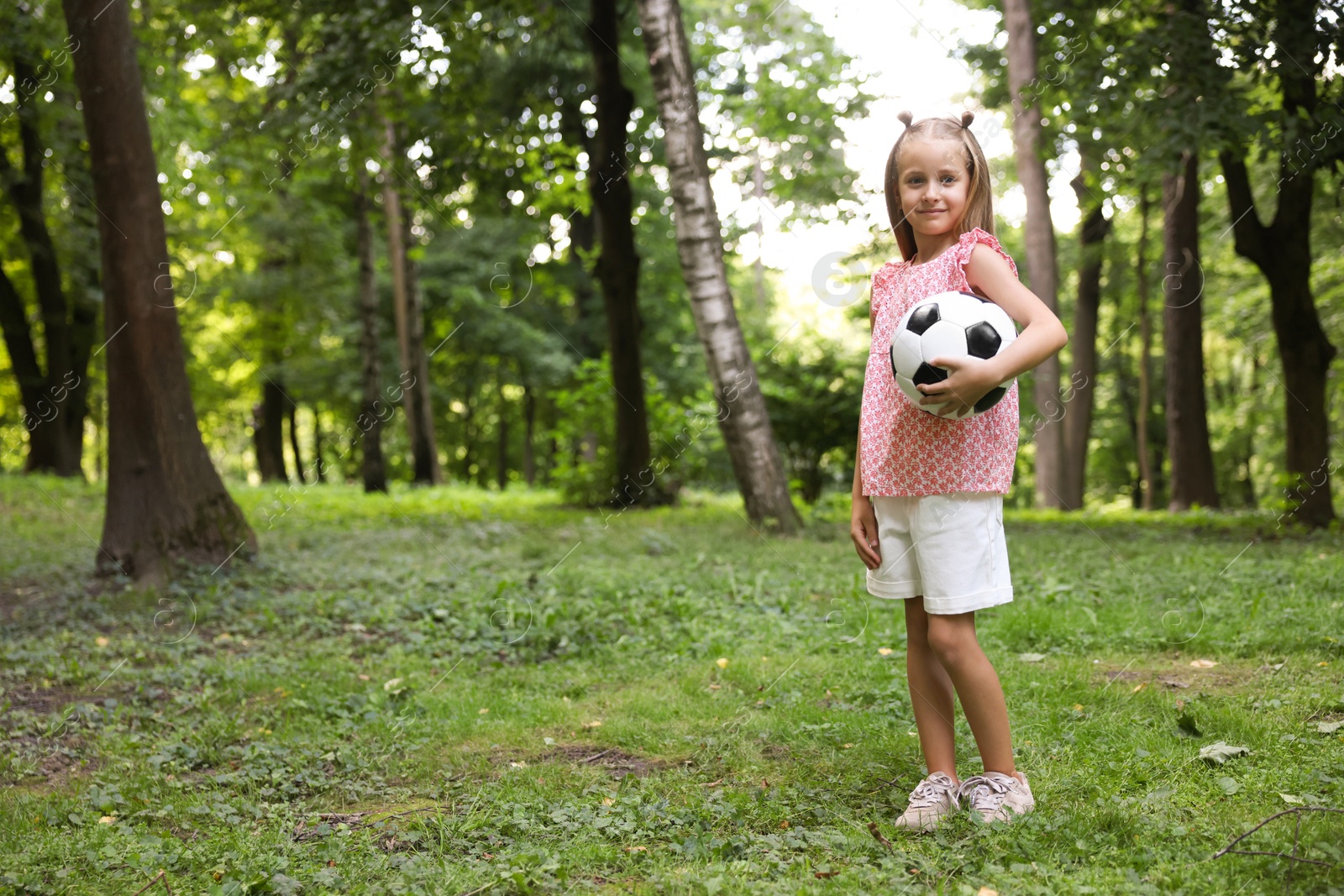 Photo of Cute little girl with soccer ball in park, space for text