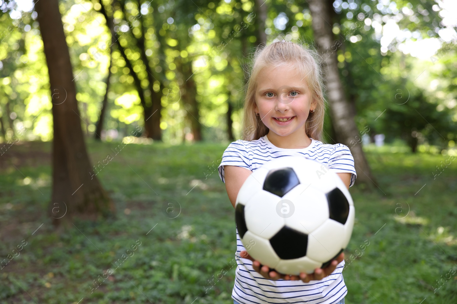 Photo of Cute little girl with soccer ball in park, space for text