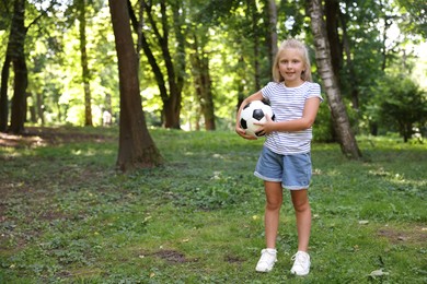 Photo of Cute little girl with soccer ball in park, space for text