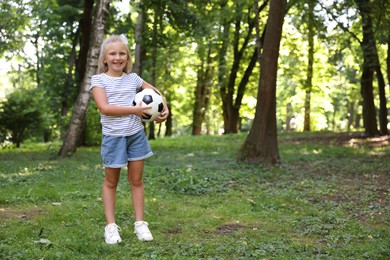 Photo of Cute little girl with soccer ball in park, space for text
