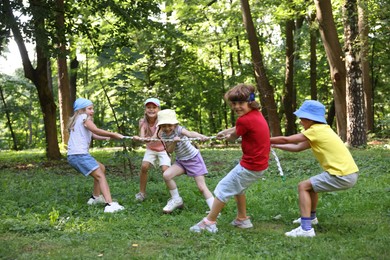 Photo of Cute little kids playing tug of war in park