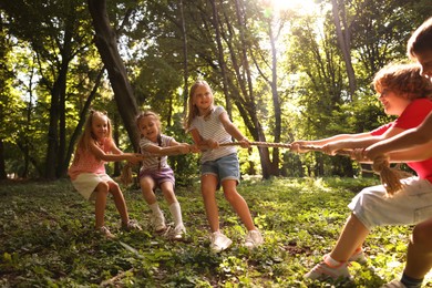 Photo of Cute little kids playing tug of war in park