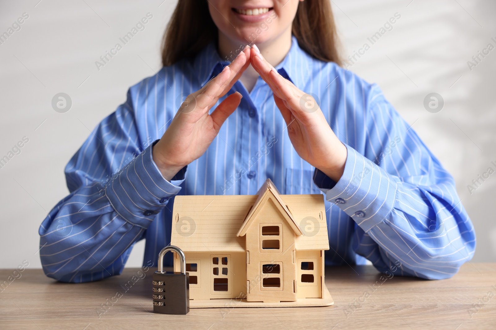 Photo of Home security. Woman protecting house model and padlock at wooden table, closeup