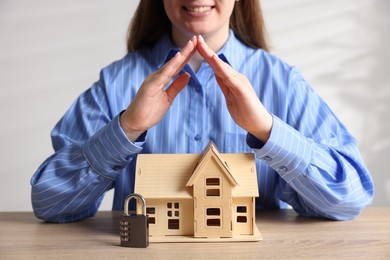 Photo of Home security. Woman protecting house model and padlock at wooden table, closeup