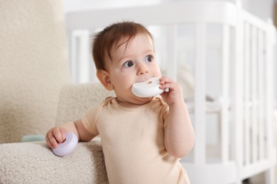 Photo of Cute little baby with toys near armchair in room