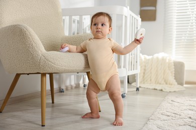 Photo of Cute little baby with toys near armchair in room