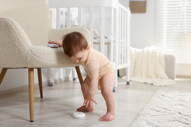 Photo of Cute little baby with toys near armchair in room