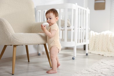 Photo of Cute little baby with toy near armchair in room