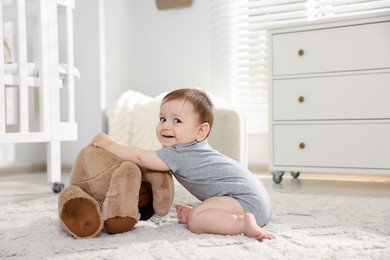 Photo of Cute little baby playing with teddy bear in room