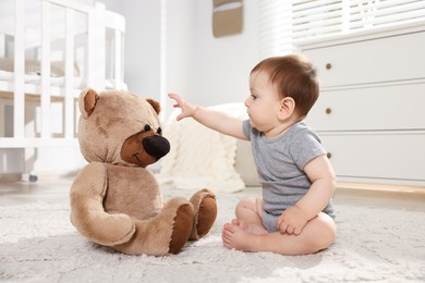 Photo of Cute little baby playing with teddy bear in room