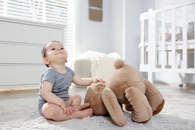 Photo of Cute little baby playing with teddy bear in room