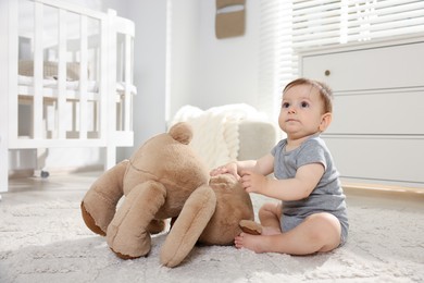 Photo of Cute little baby playing with teddy bear in room