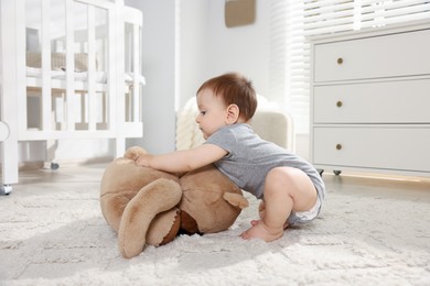 Photo of Cute little baby playing with teddy bear in room
