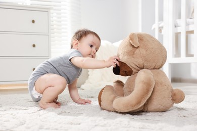 Photo of Cute little baby playing with teddy bear in room