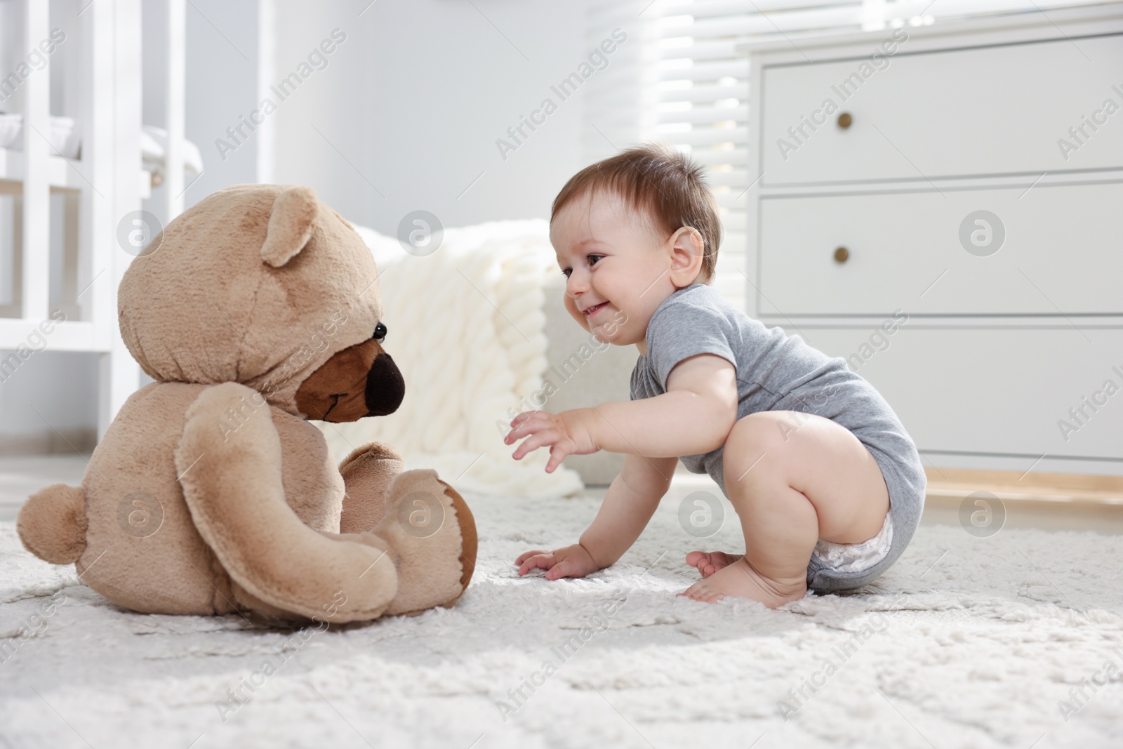 Cute little baby playing with teddy bear in room Photo of Cute little baby playing with teddy bear in room