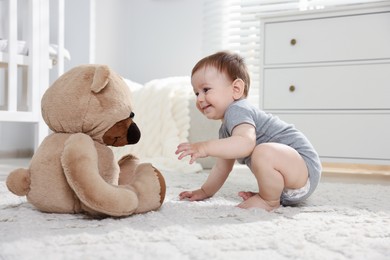 Photo of Cute little baby playing with teddy bear in room