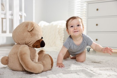Photo of Cute little baby with teddy bear in room