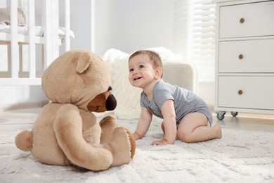 Photo of Cute little baby with teddy bear in room