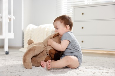 Photo of Cute little baby playing with teddy bear in room