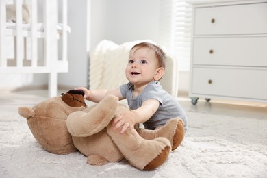 Photo of Cute little baby playing with teddy bear in room