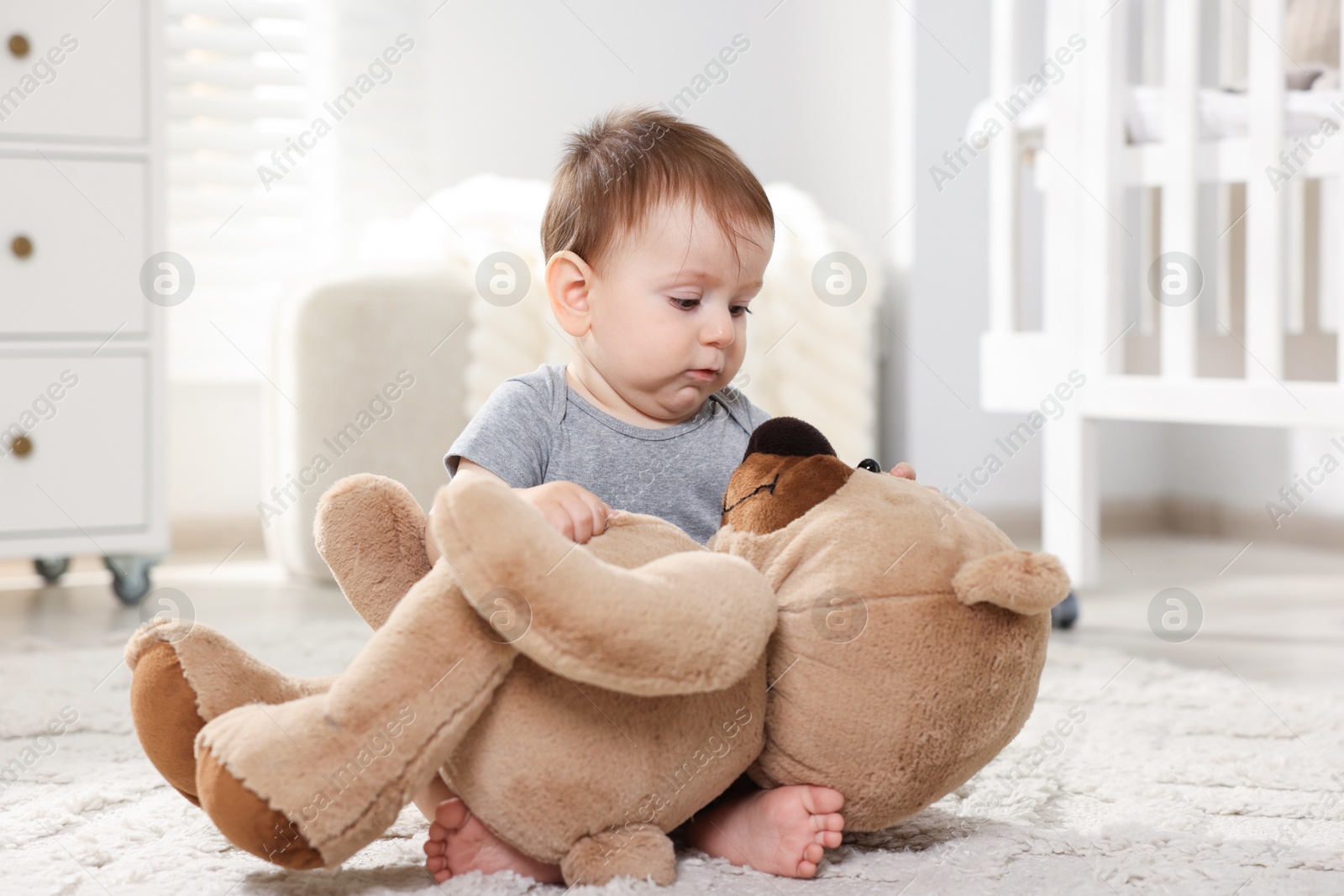 Photo of Cute little baby playing with teddy bear in room