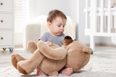Photo of Cute little baby playing with teddy bear in room