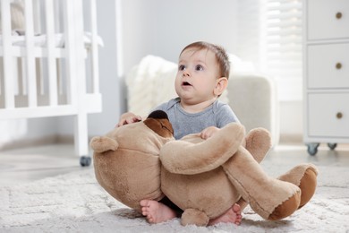 Photo of Cute little baby playing with teddy bear in room